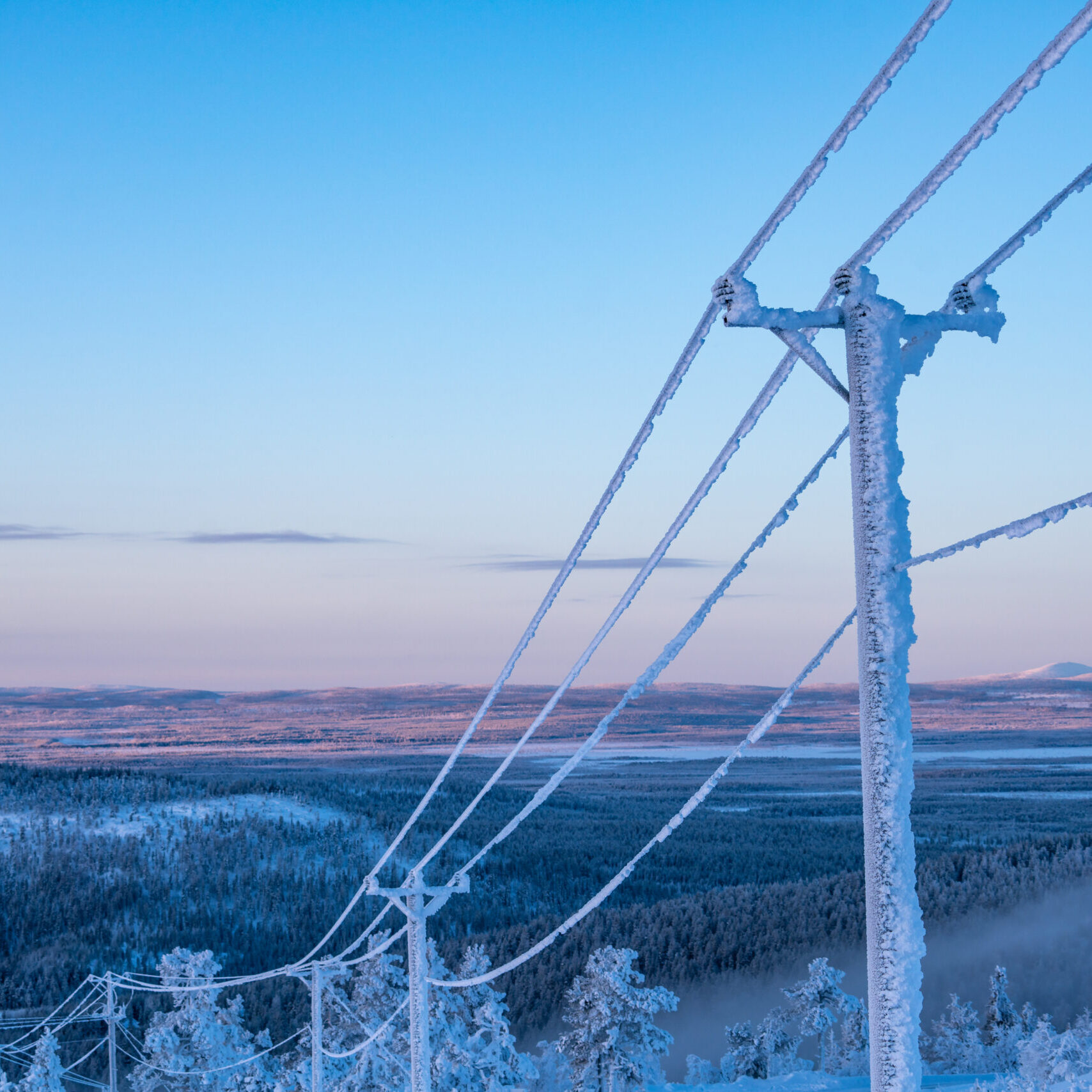 Frost and snow covered power lines during very cold winter against sky in Finland